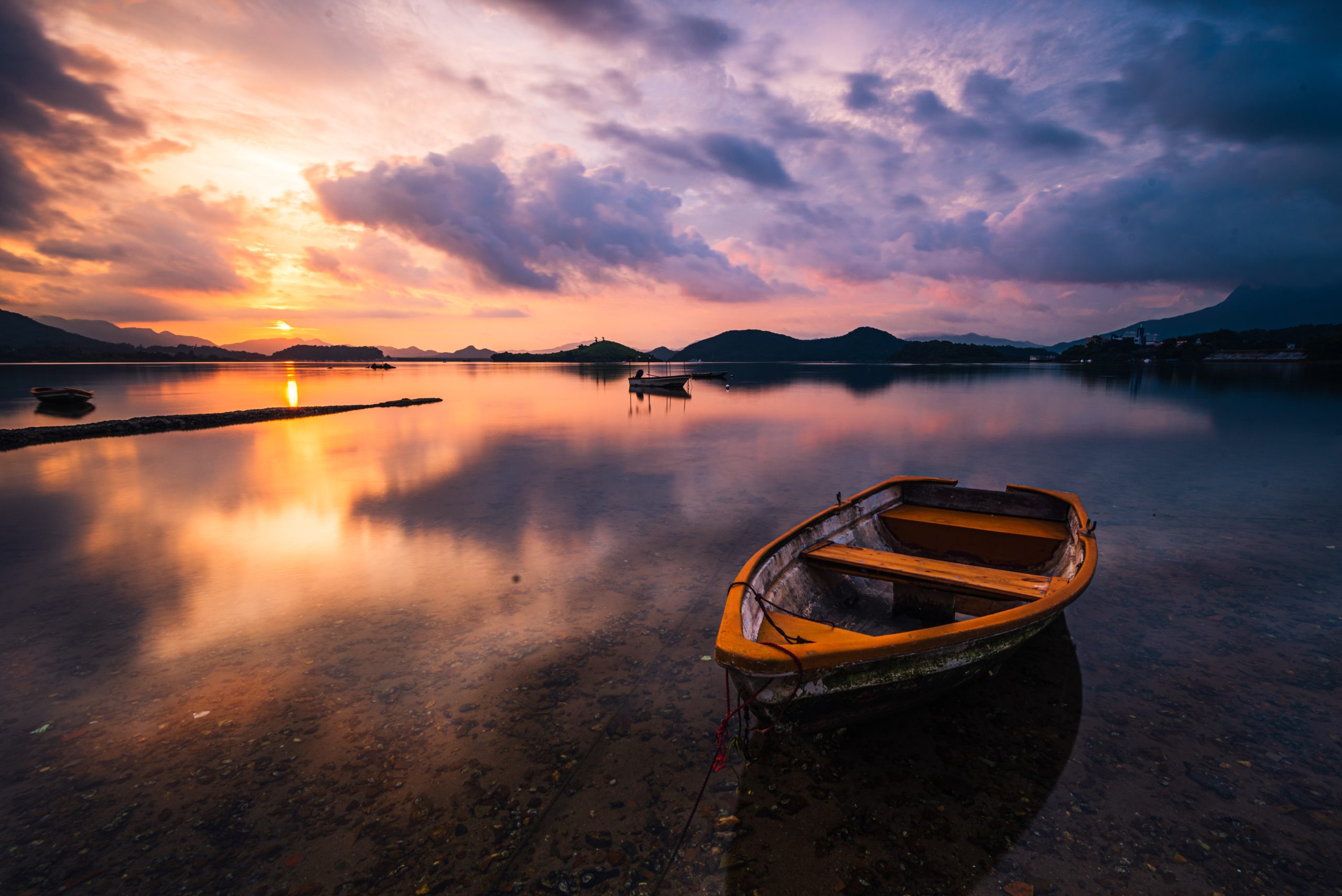 Beautiful shot of a small lake with a wooden rowboat in focus and breathtaking clouds in the sky>